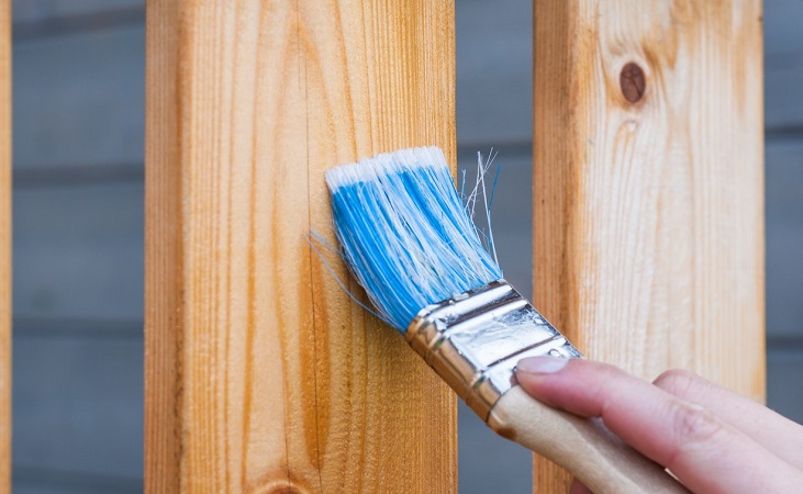 Applying a finish to wood with a blue painting brush