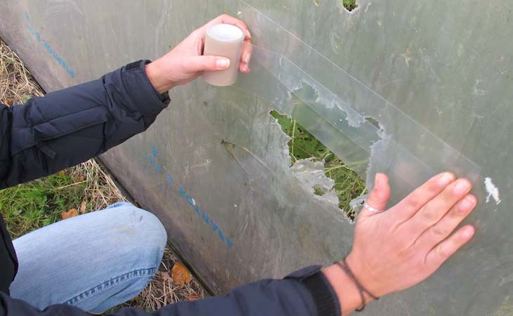 a large hole on the side of a polytunnel being fixed with tape